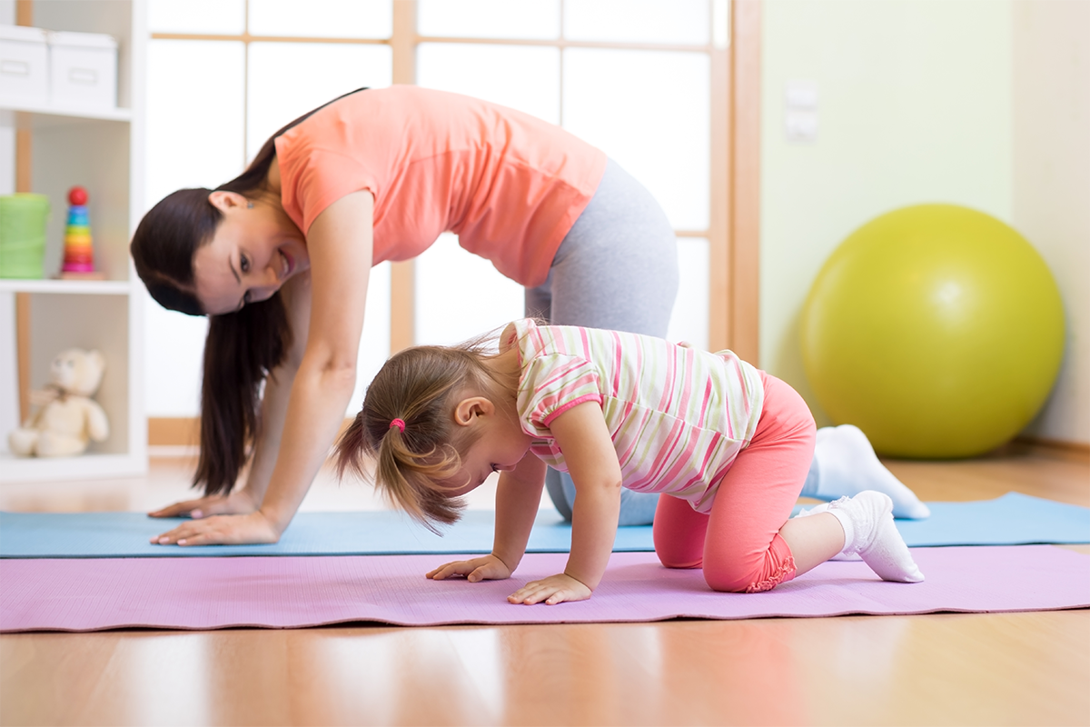 A parent and young child do a crouching cat pose on yoga mats.