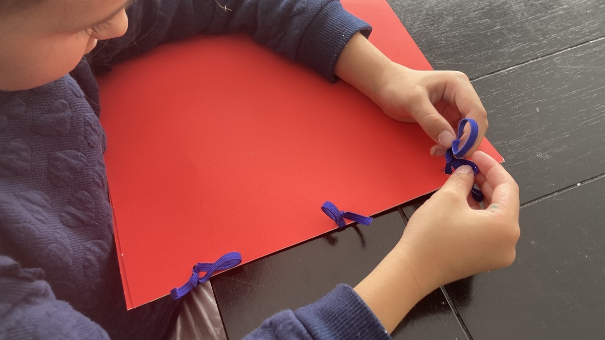 Child tying strings to attach cover to a memory book.