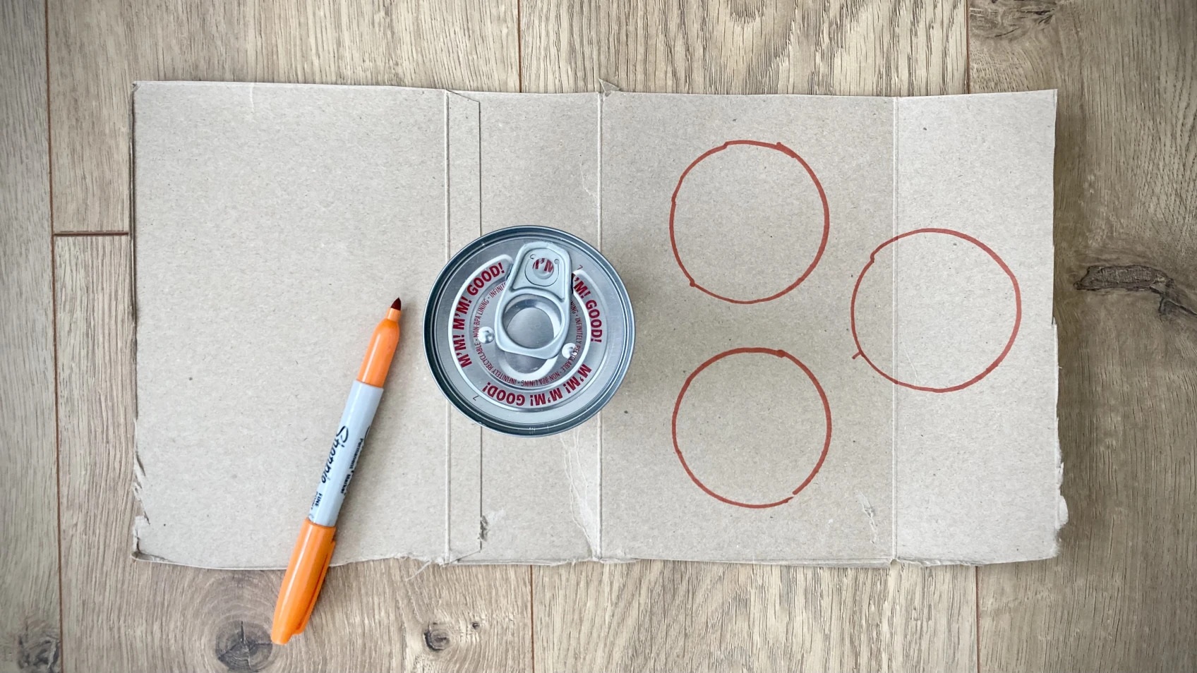 A can sits on a piece of cardboard with a sharpie tracing the can shape.