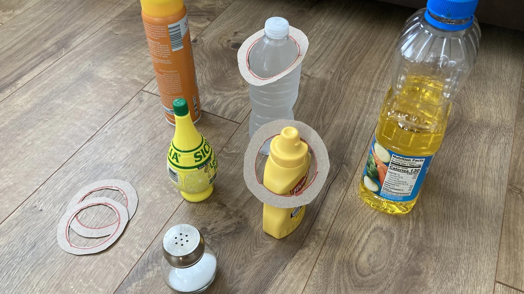 Cardboard rings sit over a water bottle and bottle of mustard.