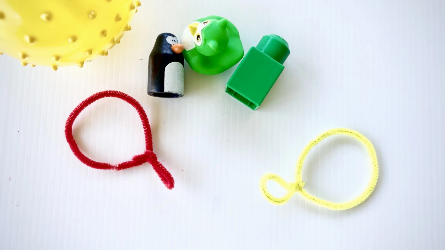Two pipe cleaners in a magnifying glass shape sit among toys.